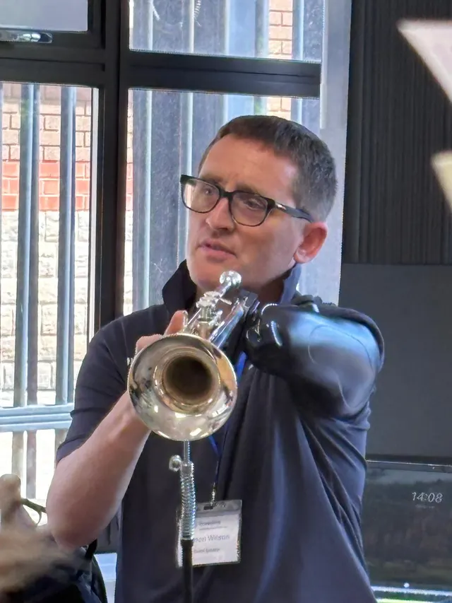 Simon playing the trumpet, supported by a stand and his prosthetic arm